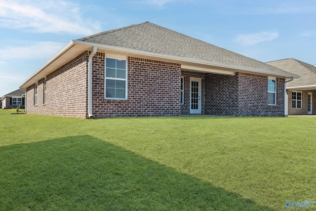 rear view of property with brick siding, a lawn, and roof with shingles