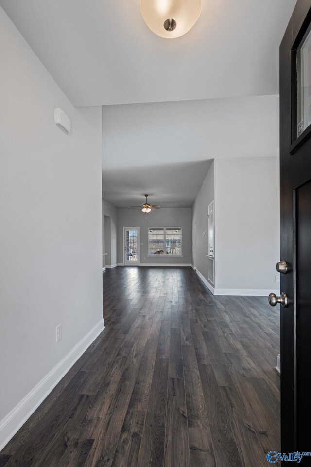 unfurnished living room with ceiling fan, dark wood-type flooring, and baseboards