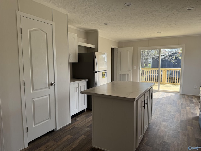 kitchen with a textured ceiling, white cabinetry, visible vents, a center island, and dark wood-style floors