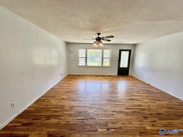 empty room with baseboards, a ceiling fan, wood finished floors, and a textured ceiling