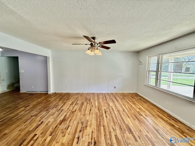 empty room featuring baseboards, a ceiling fan, light wood-style floors, and a textured ceiling