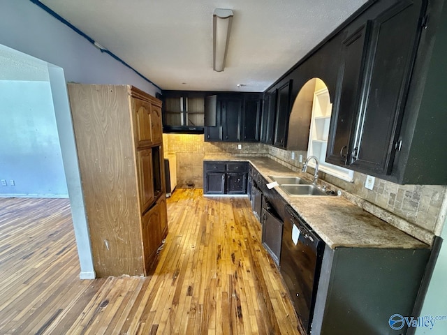 kitchen featuring dark cabinetry, black dishwasher, decorative backsplash, and a sink