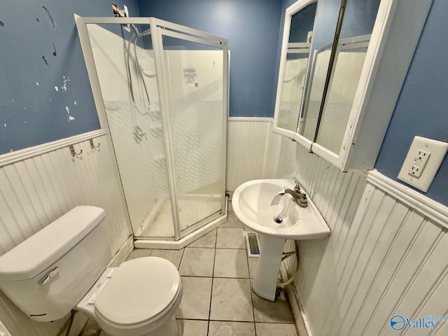 full bathroom featuring a shower stall, tile patterned floors, toilet, and a wainscoted wall
