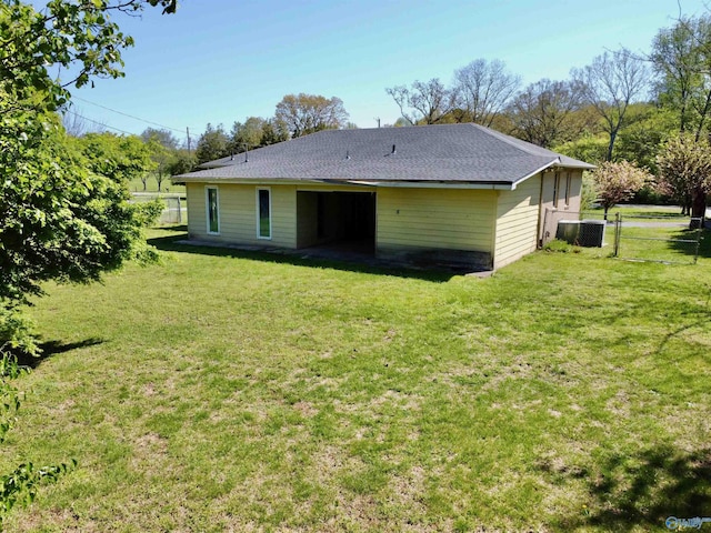 back of house featuring a shingled roof, a gate, fence, and a lawn