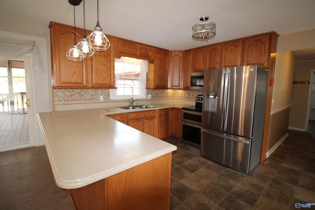 kitchen with appliances with stainless steel finishes, sink, pendant lighting, kitchen peninsula, and decorative backsplash