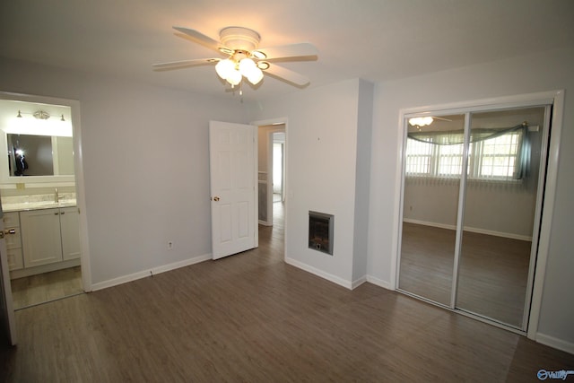 unfurnished bedroom featuring a closet, dark wood-type flooring, ceiling fan, ensuite bathroom, and sink