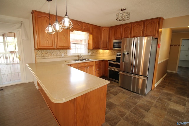 kitchen with appliances with stainless steel finishes, sink, backsplash, decorative light fixtures, and kitchen peninsula