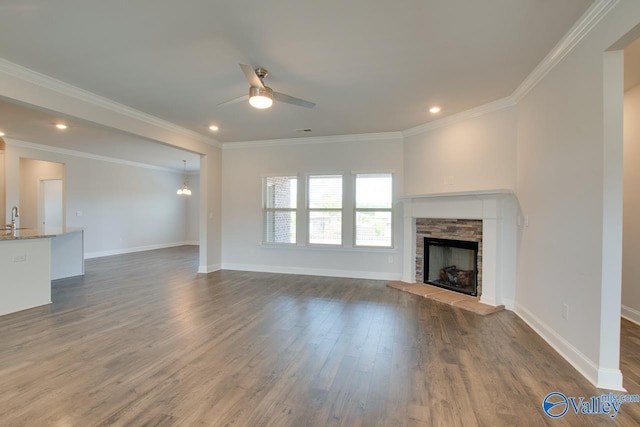 unfurnished living room featuring ceiling fan, a fireplace, wood-type flooring, and ornamental molding