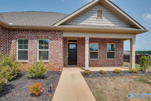 view of front of property featuring brick siding, roof with shingles, and fence