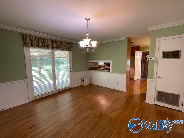 unfurnished dining area featuring wood finished floors, visible vents, crown molding, and a notable chandelier