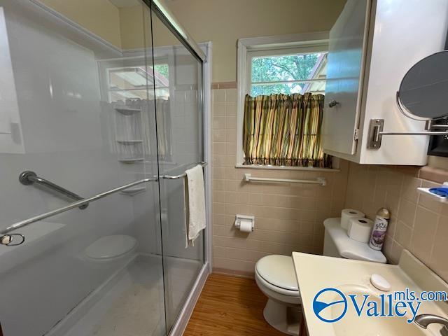full bathroom with tile walls, a stall shower, toilet, and wood finished floors