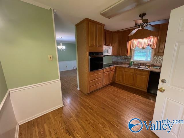 kitchen featuring brown cabinetry, tasteful backsplash, black appliances, wood finished floors, and ceiling fan with notable chandelier