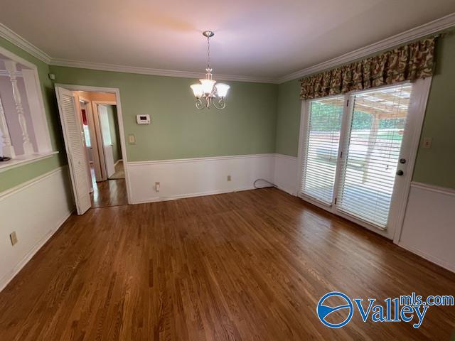 unfurnished dining area with ornamental molding, wood finished floors, and a chandelier