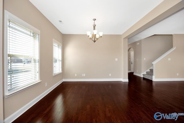 spare room featuring a notable chandelier, hardwood / wood-style flooring, arched walkways, baseboards, and stairs