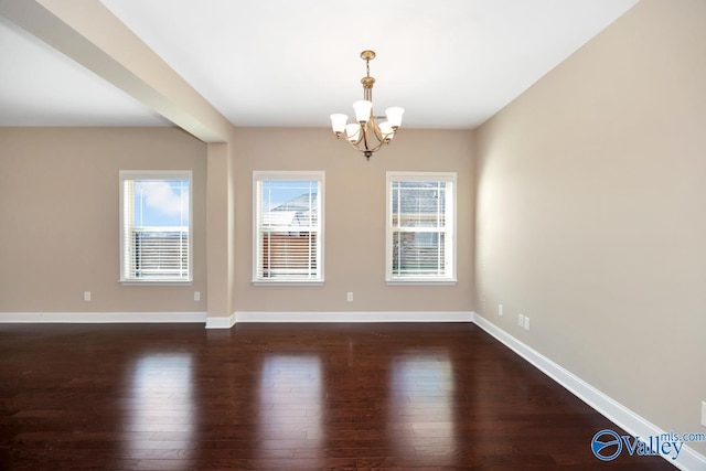 empty room with a chandelier, dark wood finished floors, baseboards, and a healthy amount of sunlight