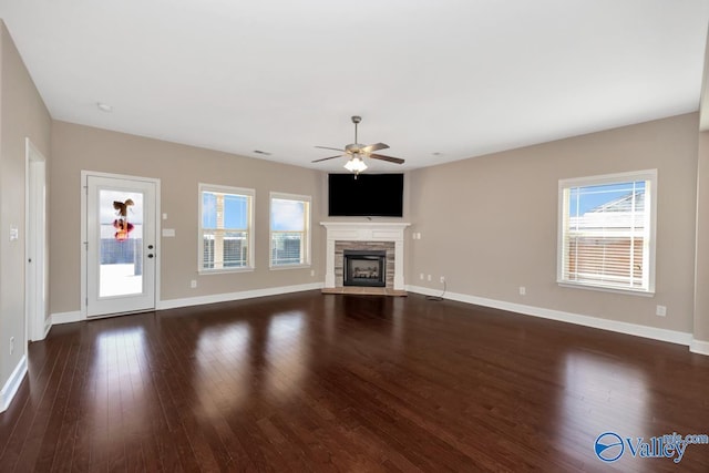 unfurnished living room featuring dark wood-type flooring, a fireplace, baseboards, and ceiling fan