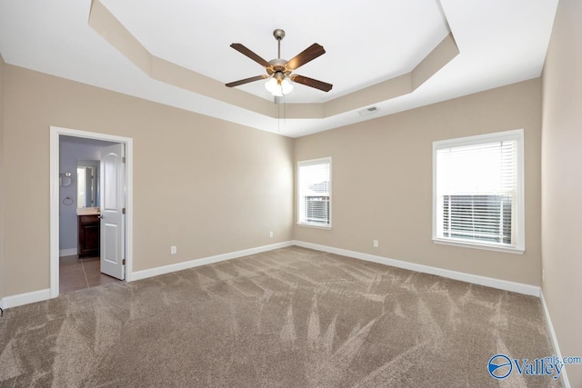 carpeted spare room with baseboards, visible vents, a ceiling fan, and a tray ceiling