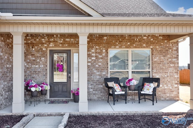 entrance to property featuring brick siding, a porch, and roof with shingles