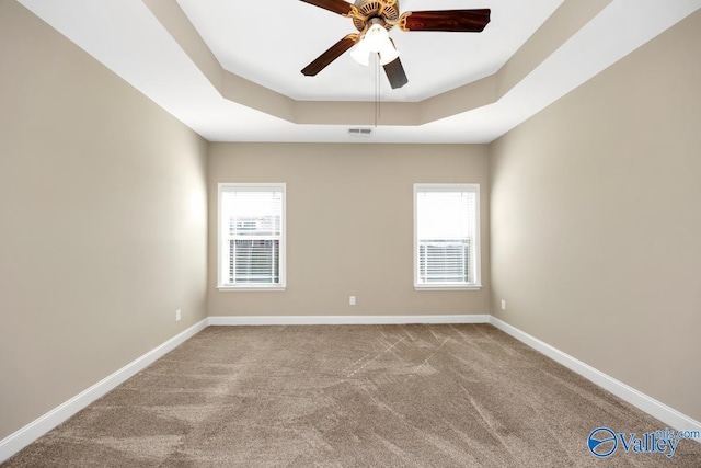 empty room with visible vents, plenty of natural light, a ceiling fan, and a tray ceiling
