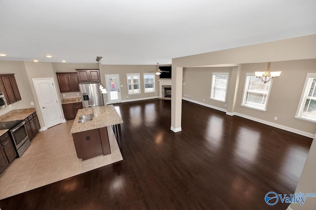 kitchen with a sink, open floor plan, appliances with stainless steel finishes, dark brown cabinets, and a chandelier