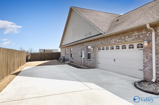 view of home's exterior featuring fence, driveway, central AC, a shingled roof, and brick siding