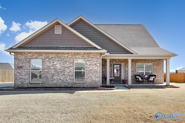 view of front of property with brick siding, covered porch, a front yard, and fence