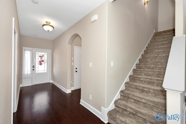 entrance foyer featuring arched walkways, stairs, baseboards, and wood finished floors