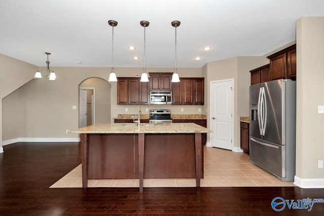 kitchen with a kitchen island with sink, arched walkways, a sink, stainless steel appliances, and light wood-style floors