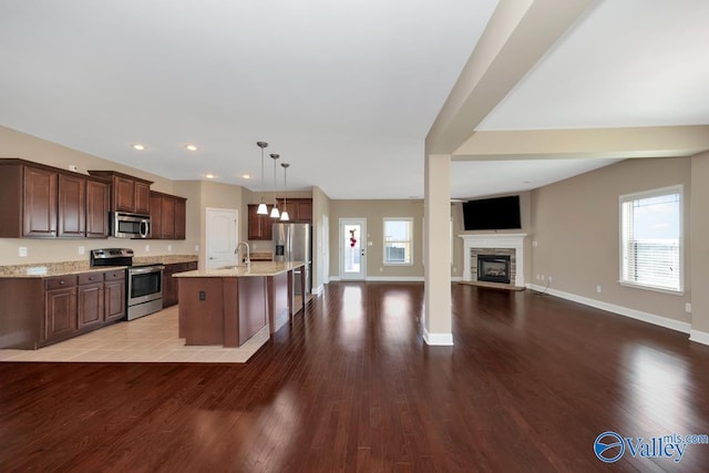 kitchen with light stone countertops, open floor plan, light wood-type flooring, appliances with stainless steel finishes, and a sink