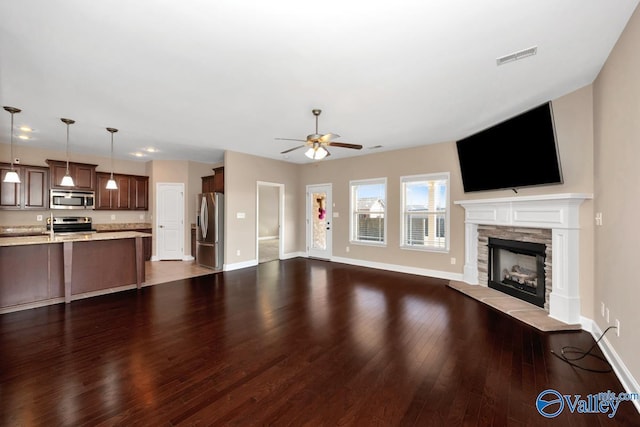 unfurnished living room with visible vents, dark wood-type flooring, a fireplace, baseboards, and ceiling fan