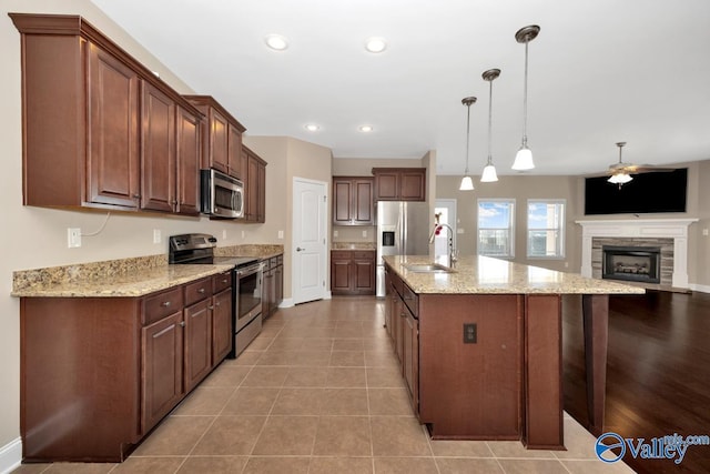 kitchen with a sink, decorative light fixtures, open floor plan, stainless steel appliances, and light tile patterned flooring