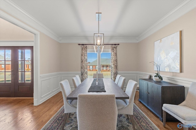 dining room featuring ornamental molding, french doors, light wood finished floors, and wainscoting