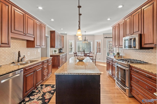 kitchen with pendant lighting, brown cabinets, appliances with stainless steel finishes, a kitchen island, and a sink