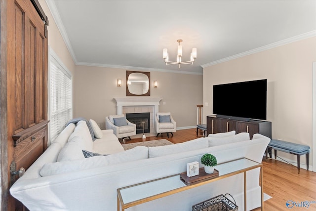 living area featuring light wood-style floors, crown molding, a tiled fireplace, and an inviting chandelier