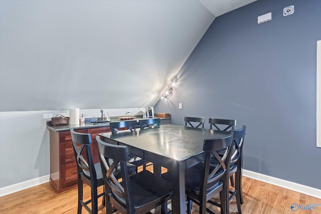 dining space featuring vaulted ceiling, light wood-style flooring, and baseboards