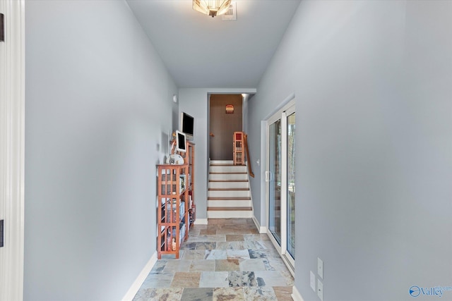 corridor with stone finish floor, baseboards, and stairs