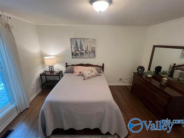 bedroom with baseboards, visible vents, dark wood finished floors, a textured ceiling, and crown molding