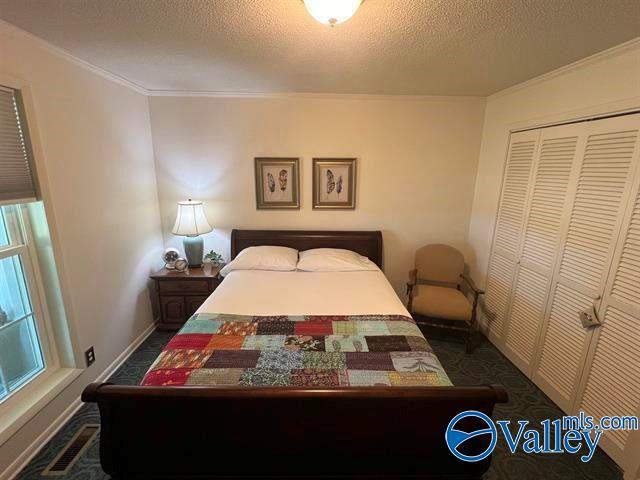 bedroom with visible vents, baseboards, ornamental molding, a closet, and a textured ceiling