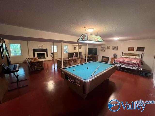 recreation room featuring billiards, a fireplace with raised hearth, concrete floors, and a textured ceiling