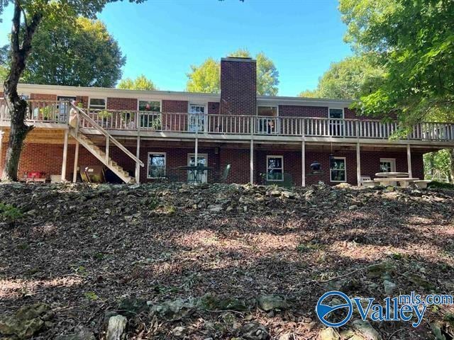 back of property with stairs, a wooden deck, brick siding, and a chimney