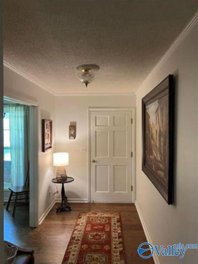 hall with a textured ceiling, wood finished floors, and ornamental molding