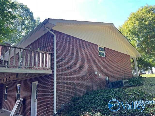 view of side of home featuring a balcony, central air condition unit, a carport, and brick siding