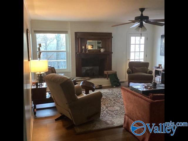 living room with a glass covered fireplace, wood finished floors, and ceiling fan