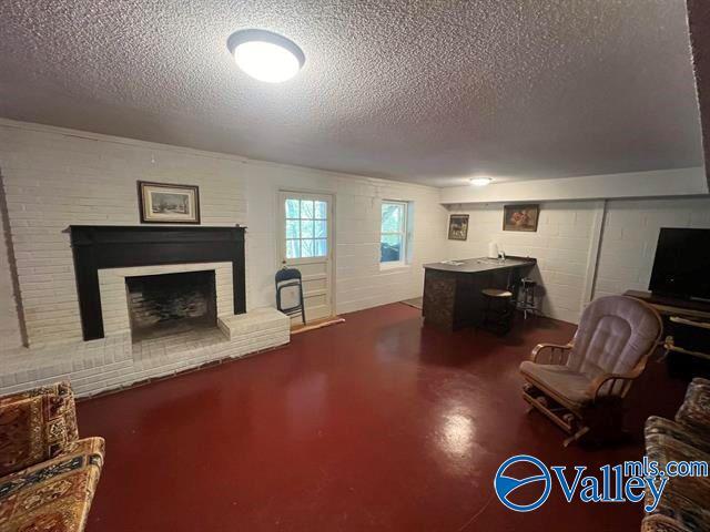 living room featuring a textured ceiling, a brick fireplace, finished concrete flooring, and concrete block wall