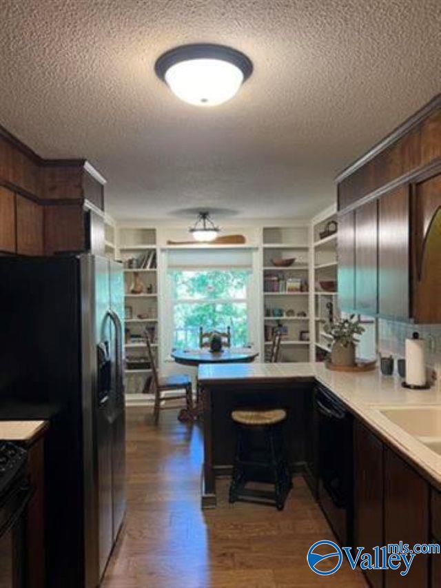 kitchen featuring fridge with ice dispenser, black dishwasher, wood finished floors, and a textured ceiling