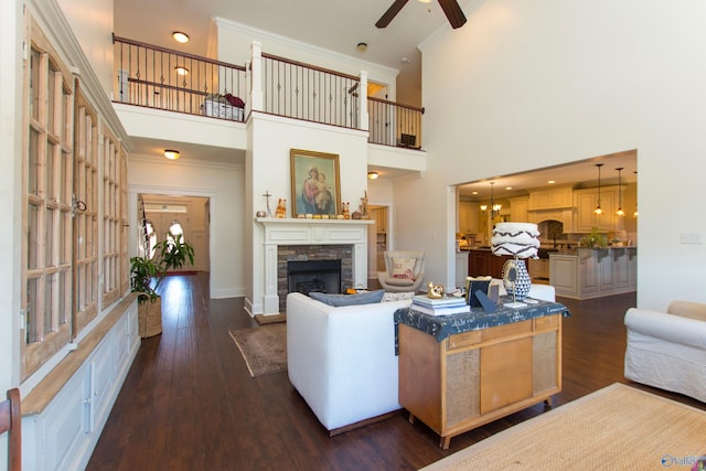 living room with ornamental molding, ceiling fan with notable chandelier, a fireplace, a towering ceiling, and dark wood-type flooring