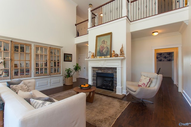 living room featuring a stone fireplace, a towering ceiling, dark hardwood / wood-style flooring, and ornamental molding