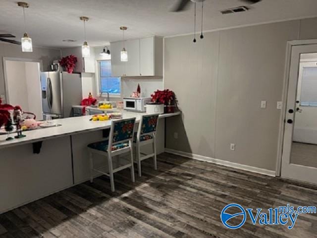 kitchen featuring stainless steel fridge, dark hardwood / wood-style flooring, a breakfast bar, ceiling fan, and white cabinets