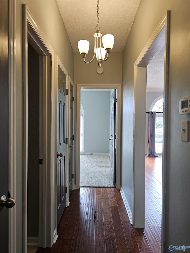 hall with baseboards, dark wood-style flooring, a textured ceiling, and a notable chandelier