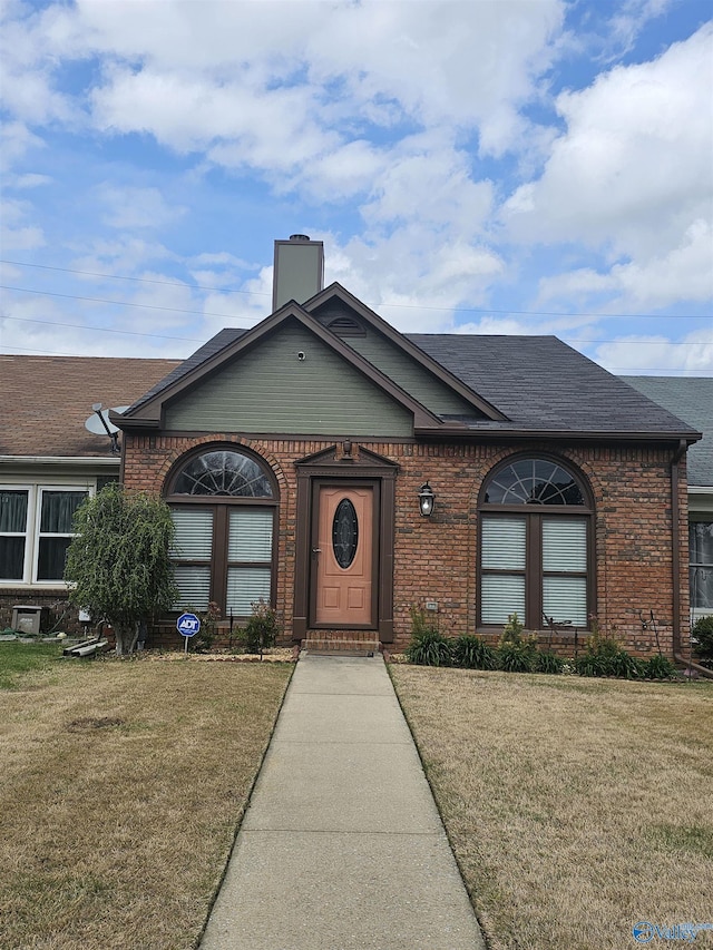 single story home with brick siding, a chimney, and a front yard